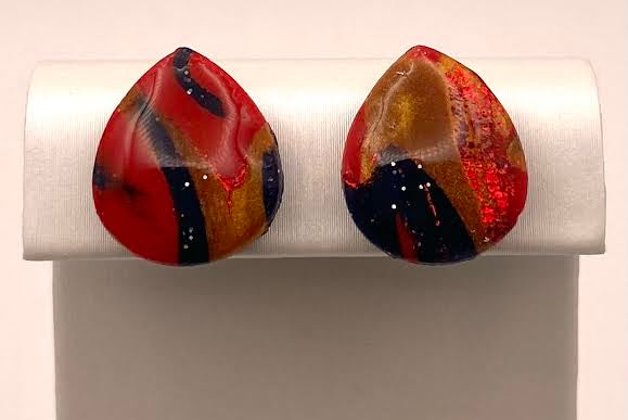 A pair of teardrop-shaped stud earrings with a marbled pattern of red, orange, black, and white, displayed on a white jewelry stand.
