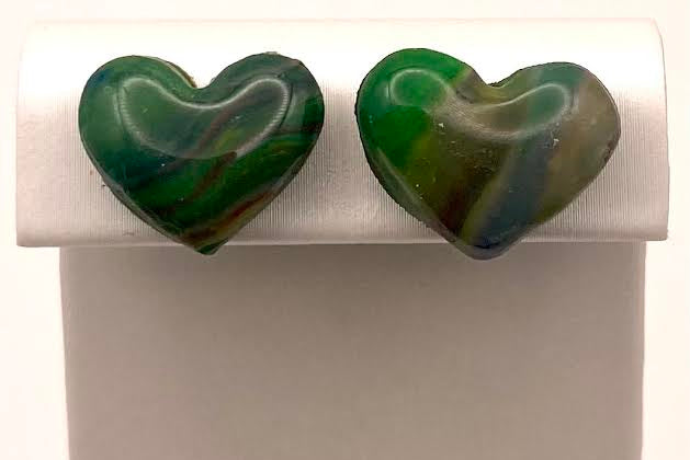 A pair of heart-shaped green marbled stud earrings displayed on a white jewelry stand against a white background.