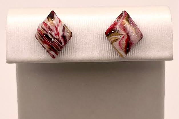 A pair of marbled glass stud earrings with swirls of red, white, and brown, displayed on a white jewelry stand against a light background.
