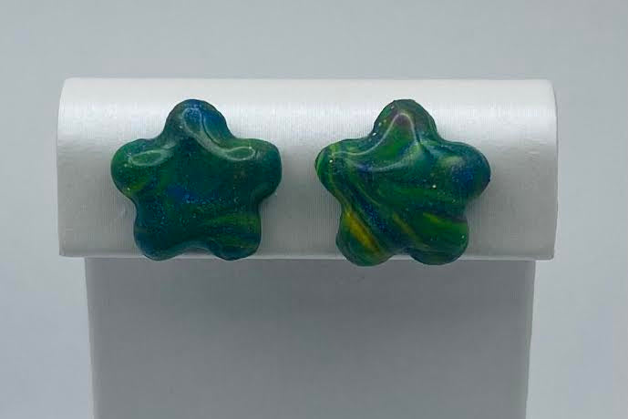 A pair of star-shaped stud earrings with a marbled green and blue glass finish, displayed on a white jewelry stand against a light gray background.