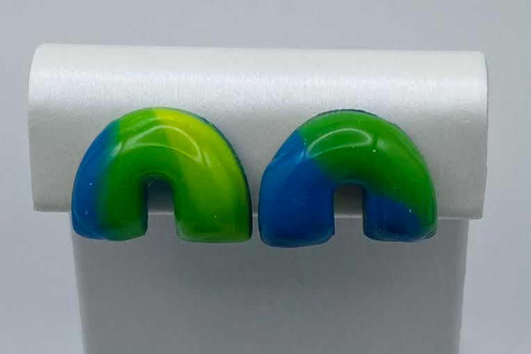 A pair of glossy, U-shaped stud earrings with a green-to-blue gradient, displayed on a white jewelry stand against a light gray background.