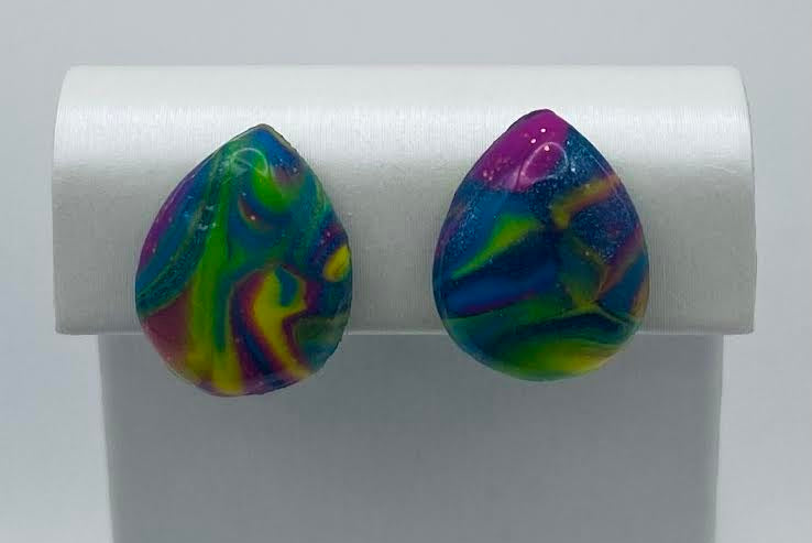 A pair of teardrop-shaped stud earrings with a vibrant, swirling marbled pattern in green, blue, purple, and yellow, displayed on a white jewelry stand.