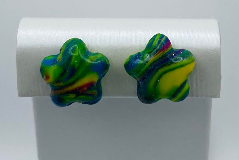 A pair of marbled star-shaped stud earrings in vibrant green, blue, yellow, and purple, displayed on a white jewelry stand.