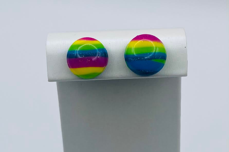 A pair of round stud earrings with horizontal rainbow stripes in pink, yellow, green, blue, and purple, displayed on a white jewelry stand against a light gray background.